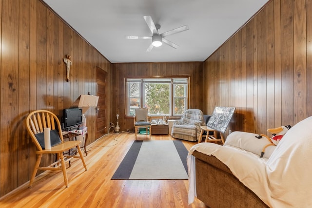 sitting room with ceiling fan, light hardwood / wood-style flooring, and wood walls