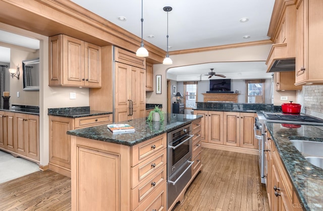 kitchen with stainless steel appliances, a kitchen island, light brown cabinetry, and hanging light fixtures