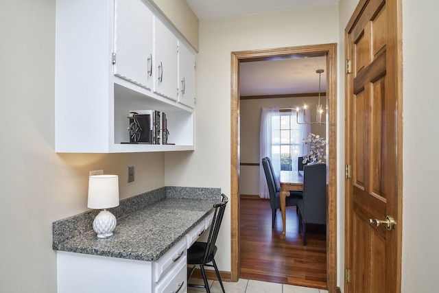 kitchen featuring white cabinetry, dark stone countertops, a notable chandelier, ornamental molding, and light hardwood / wood-style floors