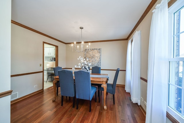 dining area with dark wood-type flooring, crown molding, and an inviting chandelier