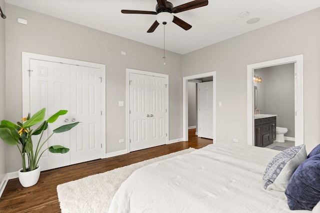 bedroom featuring connected bathroom, two closets, dark hardwood / wood-style floors, and ceiling fan