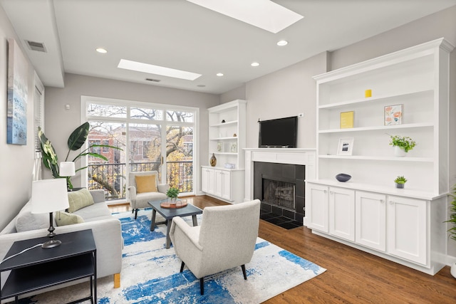 living room with a tile fireplace, dark wood-type flooring, and a skylight