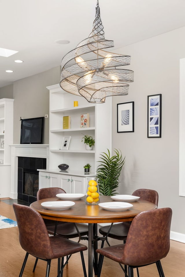 dining area with a chandelier, built in features, a tiled fireplace, and light hardwood / wood-style flooring