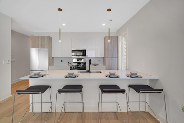 kitchen featuring sink, appliances with stainless steel finishes, white cabinetry, a kitchen bar, and decorative light fixtures