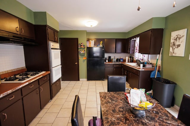 kitchen with dark brown cabinetry, sink, light tile patterned floors, white appliances, and backsplash