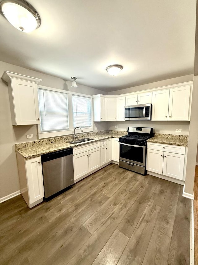 kitchen featuring sink, white cabinetry, light hardwood / wood-style flooring, stainless steel appliances, and light stone countertops