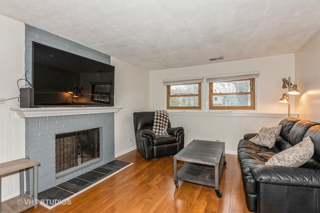 living room with a brick fireplace, visible vents, baseboards, and wood finished floors