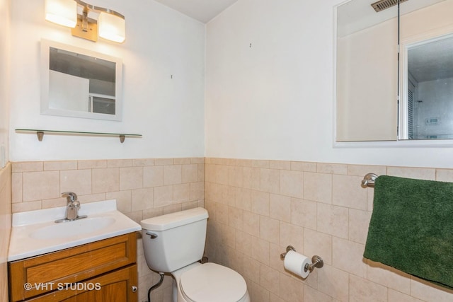 bathroom featuring wainscoting, vanity, toilet, and tile walls