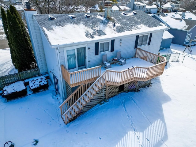 snow covered rear of property featuring stairway, roof with shingles, a chimney, and a wooden deck