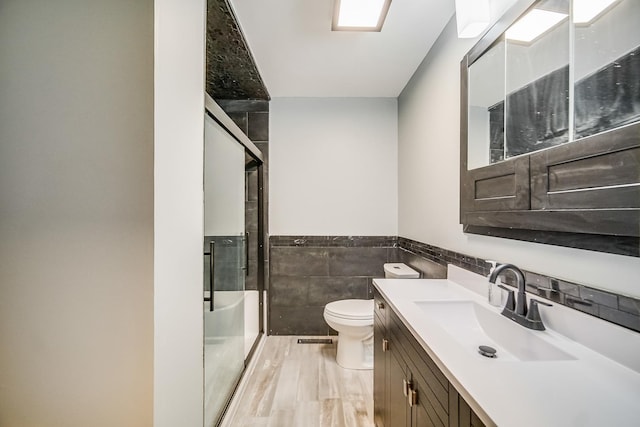 bathroom featuring vanity, toilet, a shower with shower door, and tile walls