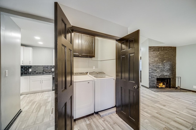 clothes washing area featuring a stone fireplace, washer and clothes dryer, and light wood-type flooring