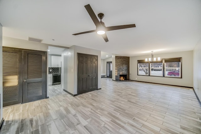 unfurnished living room with a stone fireplace, ceiling fan with notable chandelier, lofted ceiling, and light hardwood / wood-style floors