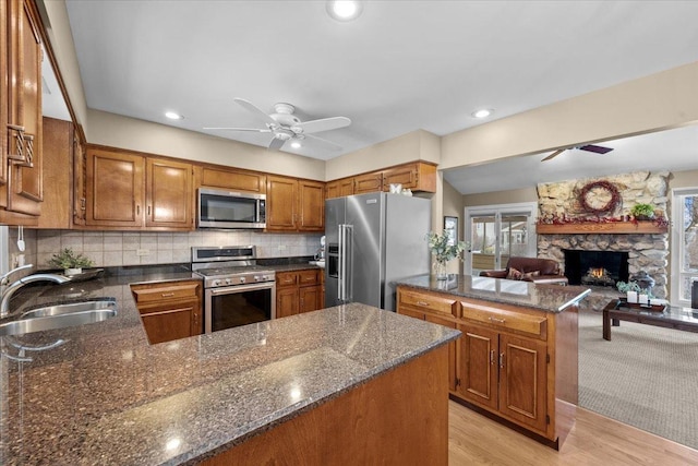 kitchen featuring sink, a stone fireplace, ceiling fan, and appliances with stainless steel finishes