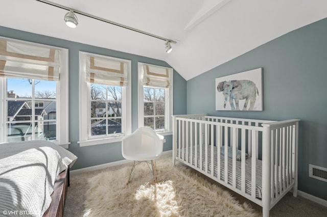 bedroom featuring vaulted ceiling, track lighting, a nursery area, and carpet