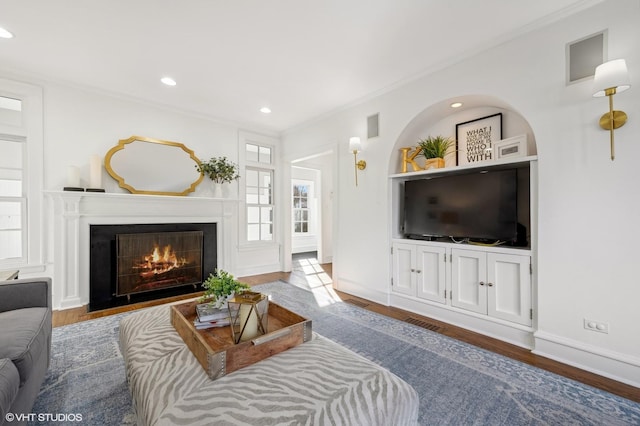 living room featuring crown molding, built in shelves, and light hardwood / wood-style flooring