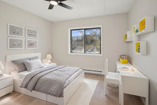 bedroom featuring ceiling fan, light hardwood / wood-style flooring, and a baseboard heating unit