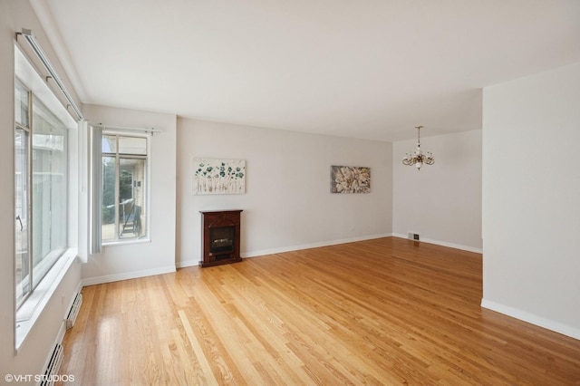 unfurnished living room with light wood-type flooring, baseboards, an inviting chandelier, and a fireplace