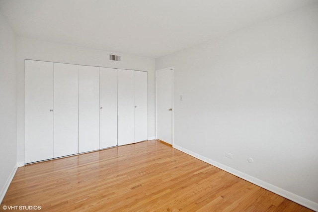 unfurnished bedroom featuring light wood-type flooring, visible vents, baseboards, and a closet