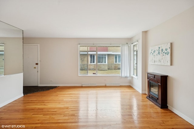 unfurnished living room featuring a glass covered fireplace, baseboards, light wood-type flooring, and a baseboard radiator