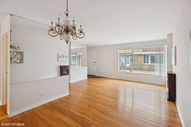 unfurnished living room with baseboards, a notable chandelier, and light wood finished floors