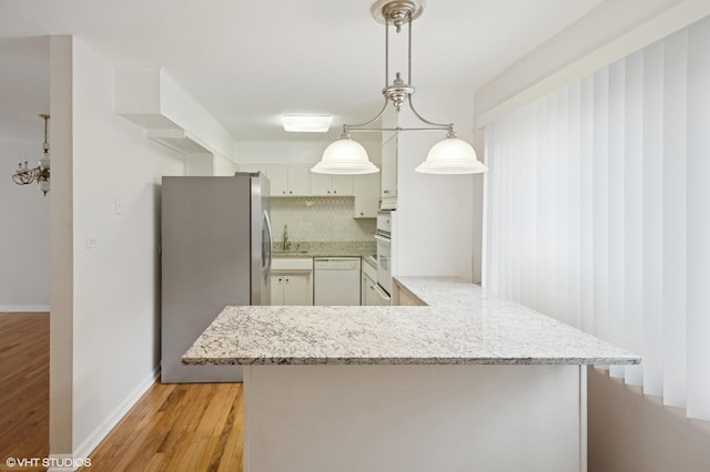 kitchen with light stone counters, dishwasher, freestanding refrigerator, and light wood-style floors