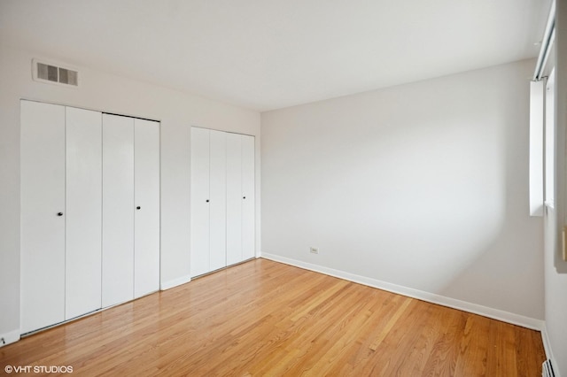 unfurnished bedroom featuring visible vents, baseboards, light wood-type flooring, and multiple closets