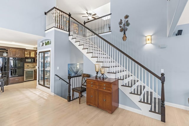 stairway featuring hardwood / wood-style flooring, beverage cooler, ceiling fan, and a high ceiling