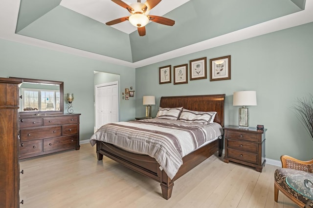 bedroom featuring a tray ceiling, a closet, ceiling fan, and light wood-type flooring