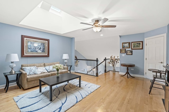 living room with a skylight, ceiling fan, and light wood-type flooring