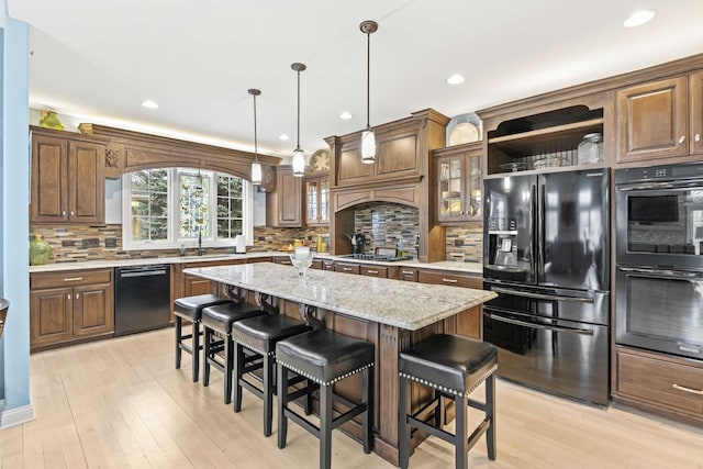 kitchen featuring a kitchen breakfast bar, a center island, light stone counters, black appliances, and decorative light fixtures