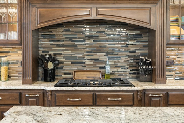 kitchen with tasteful backsplash, light stone countertops, dark brown cabinetry, and black gas cooktop