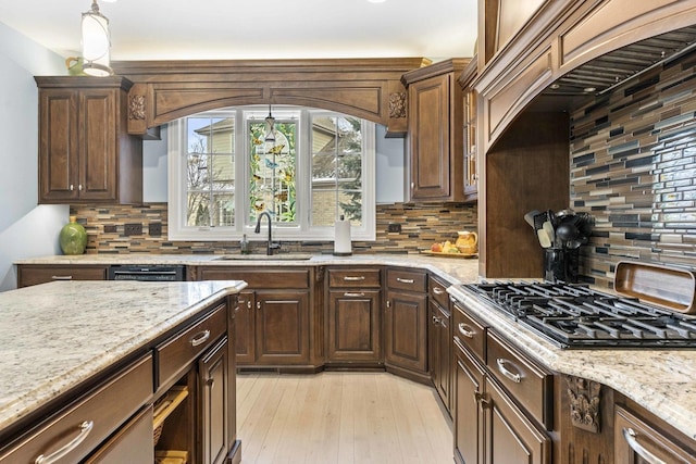 kitchen with stainless steel gas stovetop, tasteful backsplash, sink, light stone counters, and light wood-type flooring