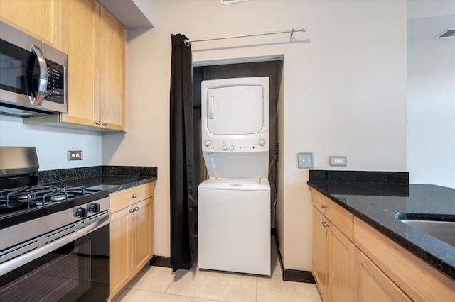 kitchen with stacked washer and dryer, light tile patterned floors, stainless steel appliances, and dark stone counters