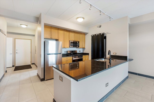 kitchen with appliances with stainless steel finishes, sink, dark stone countertops, light tile patterned floors, and track lighting