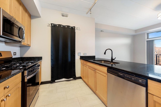 kitchen with appliances with stainless steel finishes, sink, dark stone countertops, kitchen peninsula, and light brown cabinets