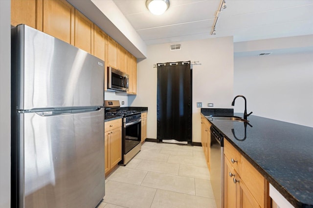 kitchen with rail lighting, sink, light tile patterned floors, dark stone countertops, and stainless steel appliances