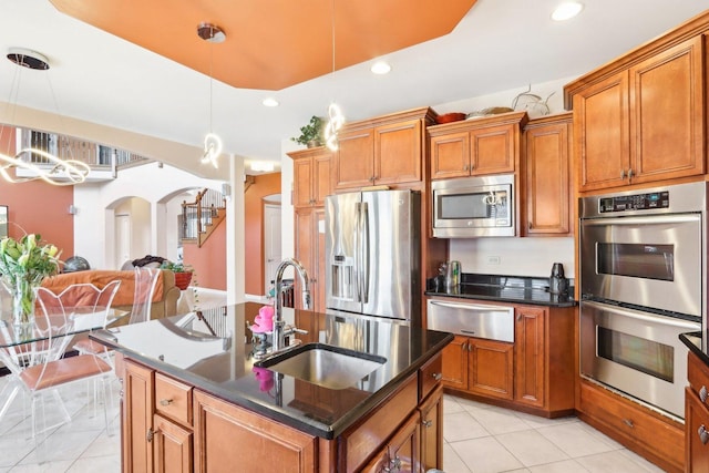 kitchen featuring appliances with stainless steel finishes, decorative light fixtures, an island with sink, sink, and light tile patterned floors