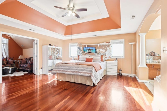 bedroom featuring a raised ceiling, decorative columns, and hardwood / wood-style floors