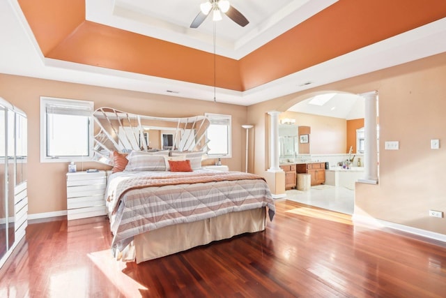 bedroom with wood-type flooring, a tray ceiling, multiple windows, and ornate columns