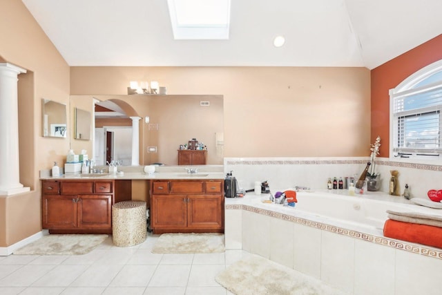 bathroom with decorative columns, a skylight, vanity, tiled tub, and tile patterned flooring