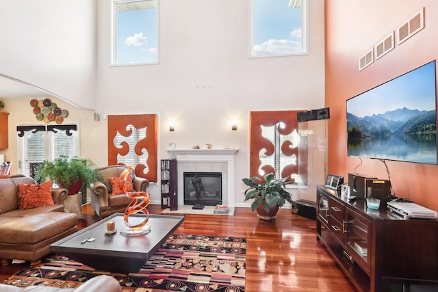 living room with hardwood / wood-style flooring, a towering ceiling, and a tiled fireplace