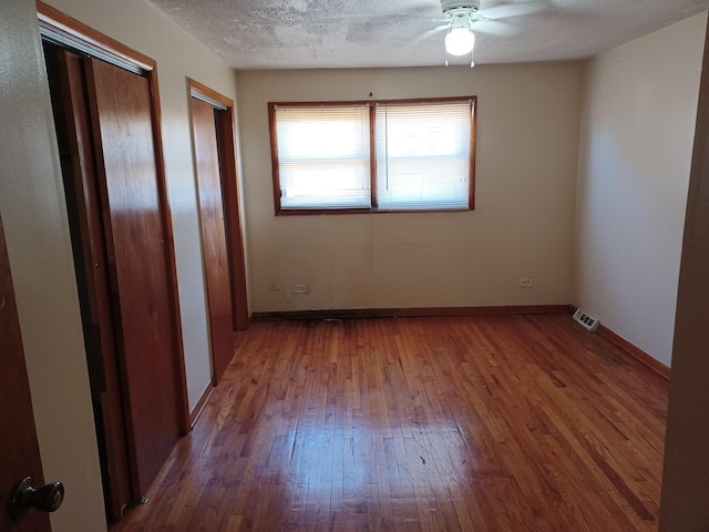 empty room with ceiling fan, wood-type flooring, and a textured ceiling