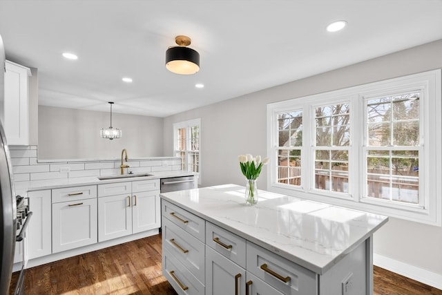 kitchen with decorative light fixtures, white cabinetry, sink, a center island, and light stone countertops