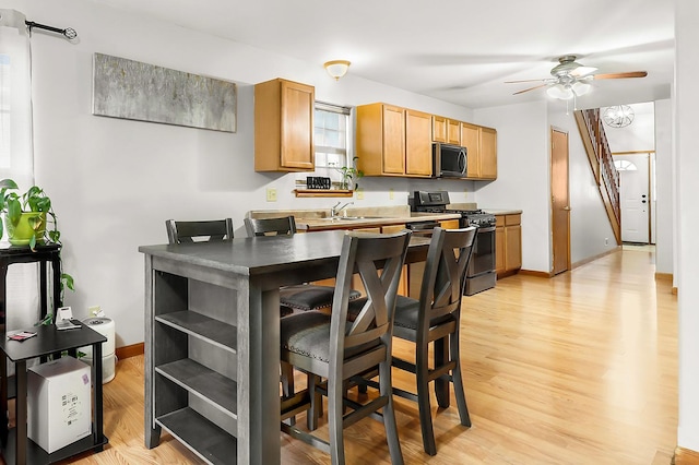 kitchen with a breakfast bar, sink, light wood-type flooring, ceiling fan, and stainless steel appliances