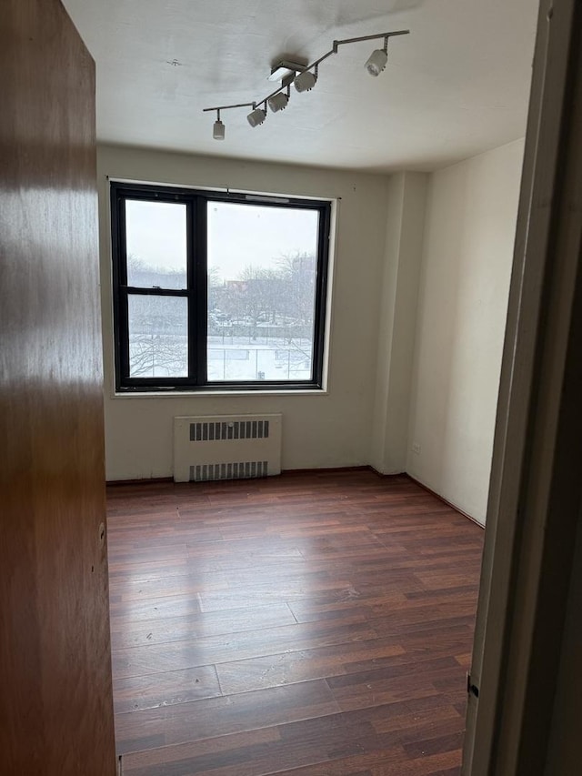 unfurnished room with dark hardwood / wood-style flooring, radiator, and a wealth of natural light