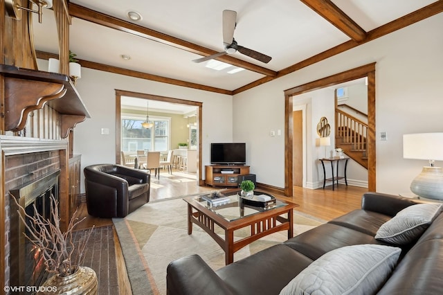 living room featuring ceiling fan, a fireplace, beam ceiling, and light hardwood / wood-style flooring