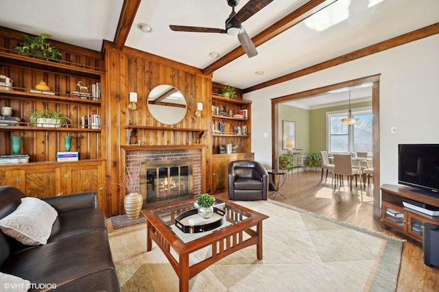 living room with ceiling fan, beam ceiling, a brick fireplace, and light wood-type flooring