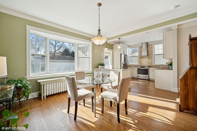 dining area with ornamental molding, radiator heating unit, and light hardwood / wood-style flooring