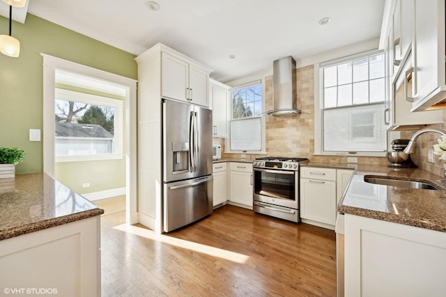 kitchen featuring sink, white cabinetry, dark stone counters, stainless steel appliances, and wall chimney range hood