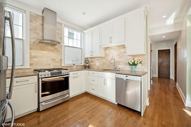 kitchen with wall chimney range hood, sink, appliances with stainless steel finishes, light stone countertops, and white cabinets